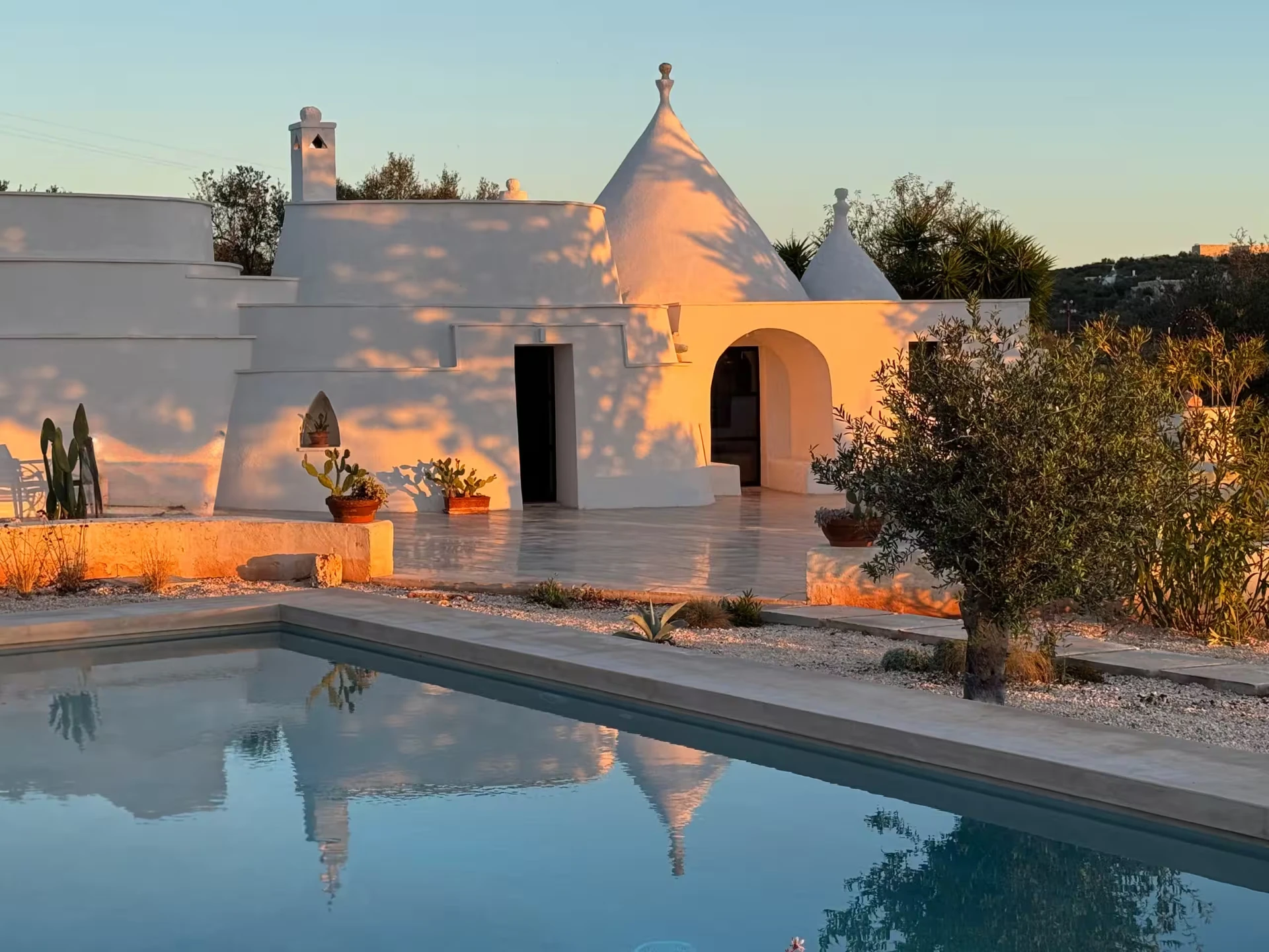 Trulli Lumena at sunset — white stone trullo reflected in a quiet pool