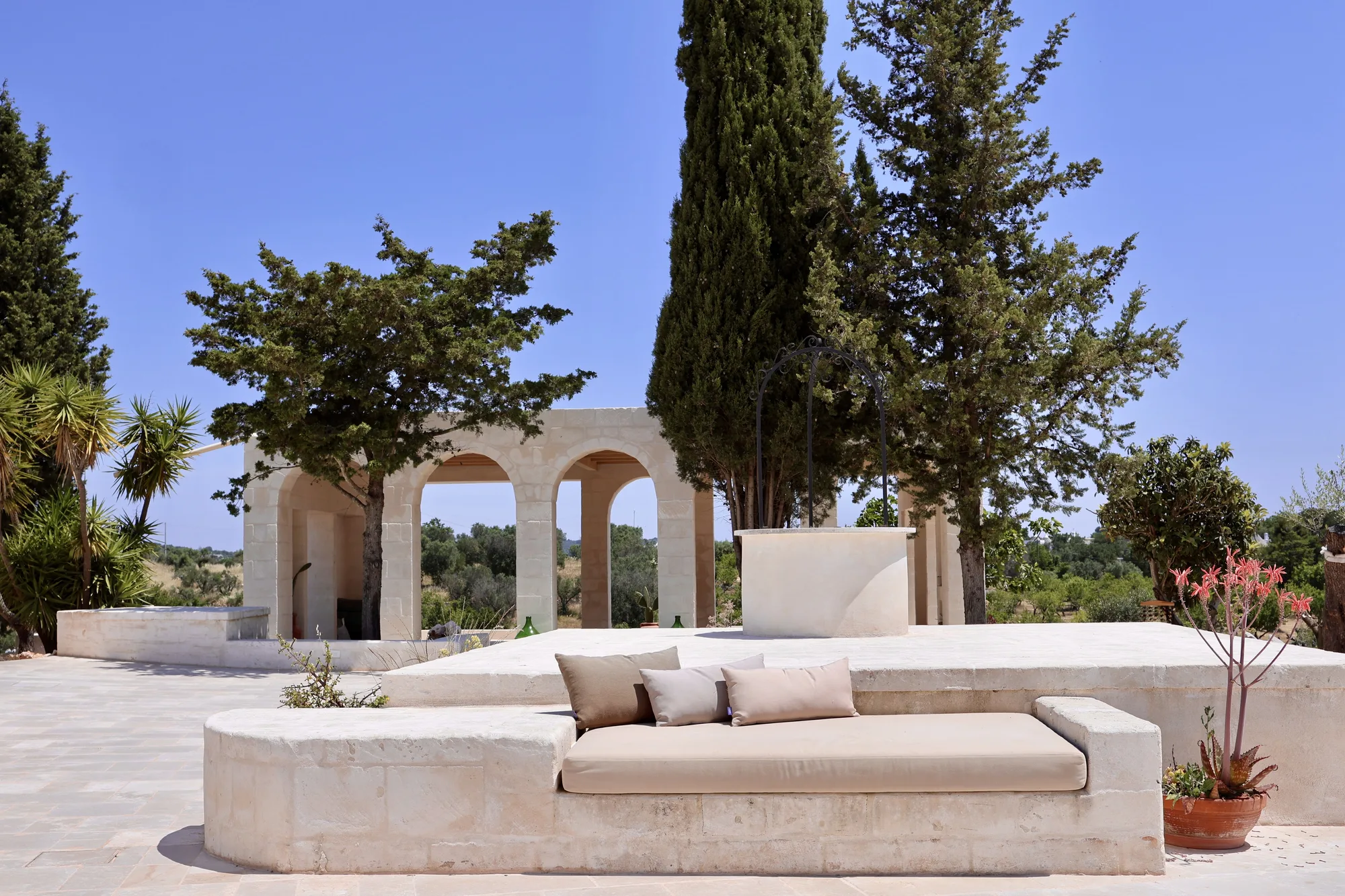 Stone courtyard with the old well and a cypress over the Valle d'Itria
