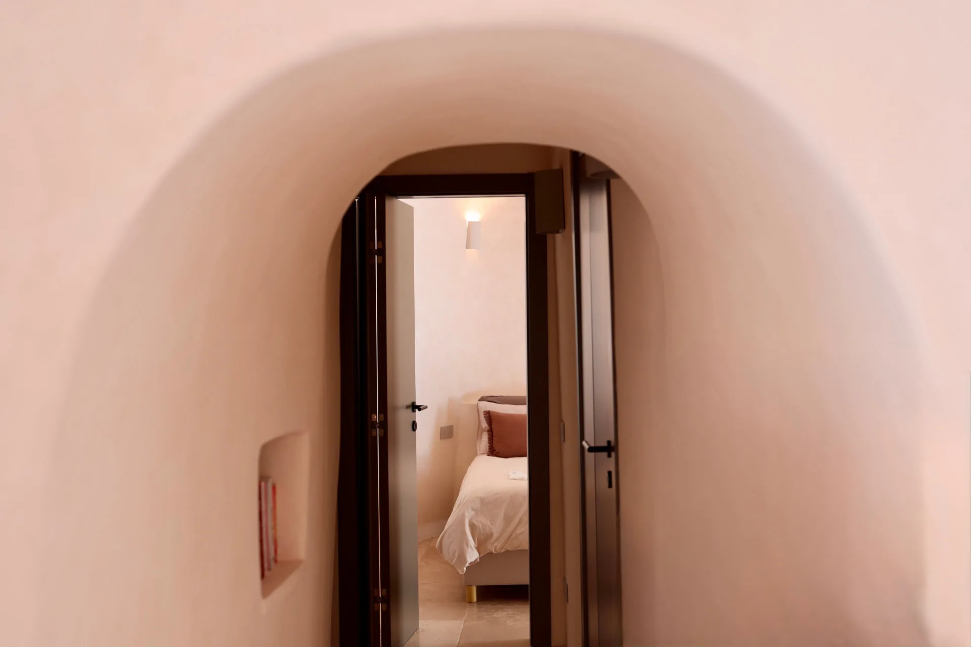 Sunset suite seen through the arched stone passage, bed lit by a wall light